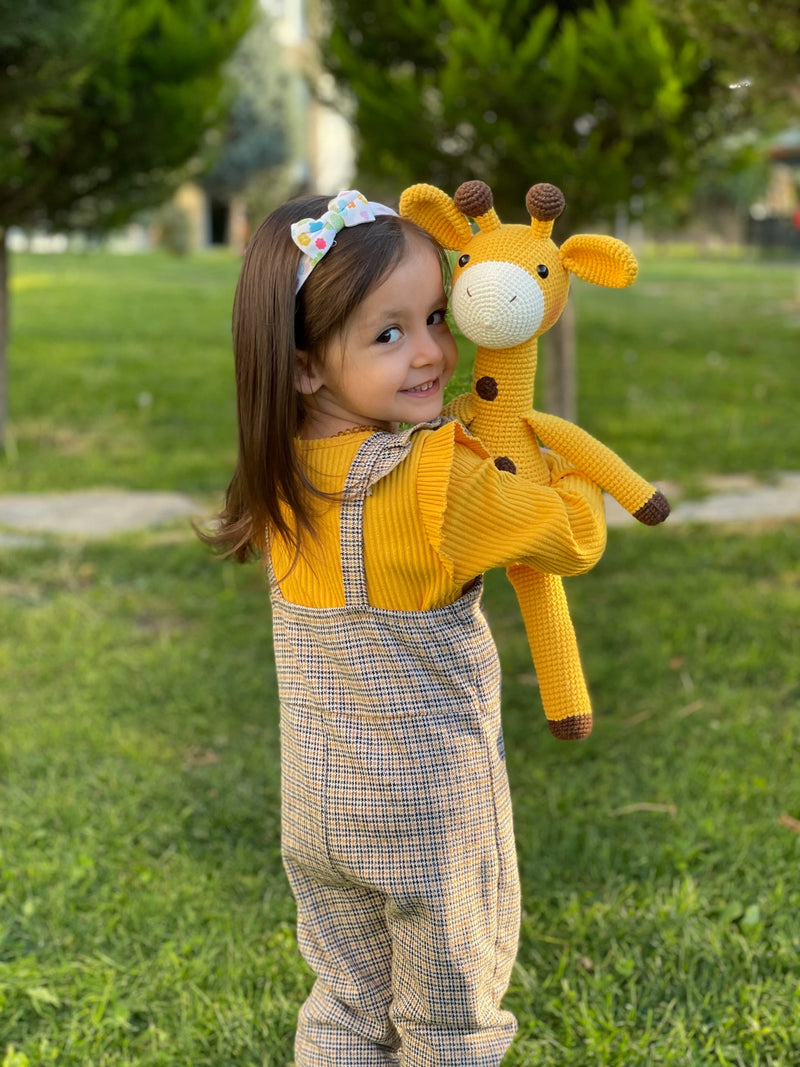 A cute handmade crocheted yellow giraffe toy held by a smiling child, made using the amigurumi technique, with customizable name on a leather label. Perfect for baby showers and personalized gifts.