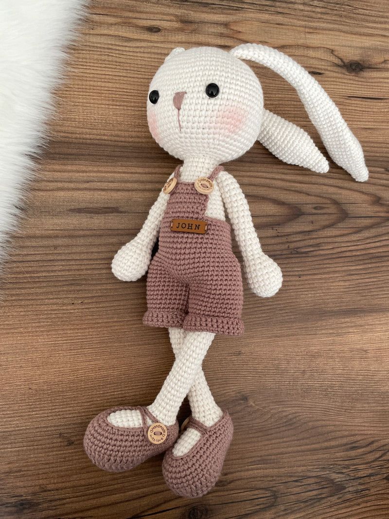 Handmade mink color overall bunny rabbit toy, crocheted using amigurumi technique with long ears and a custom name on a leather label, perfect for gifts.