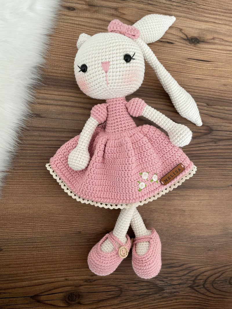 Handmade crochet Pink Dressed Bunny Rabbit Toy, featuring long ears, a pink dress with floral details, and personalized with a name on a leather label.