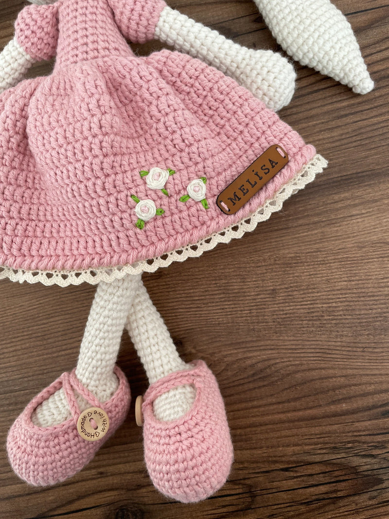 Handmade crochet Pink Dressed Bunny Rabbit Toy, featuring long ears, a pink dress with floral details, and personalized with a name on a leather label.