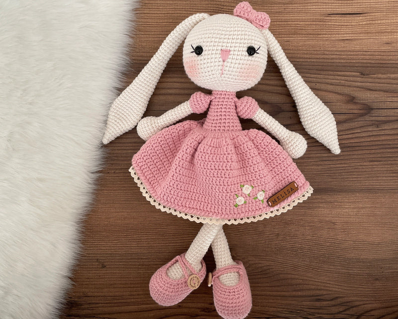 Handmade crochet Pink Dressed Bunny Rabbit Toy, featuring long ears, a pink dress with floral details, and personalized with a name on a leather label, perfect for unique girl gifts and imaginative play.