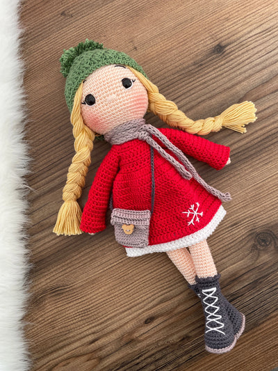 Handmade crocheted Red Snowflake Girl Doll featuring a red dress, snowflake detail, and a cute braided hairstyle. Customizable with a name on a leather label, made using amigurumi techniques. Perfect as a personalized gift or nursery decor.