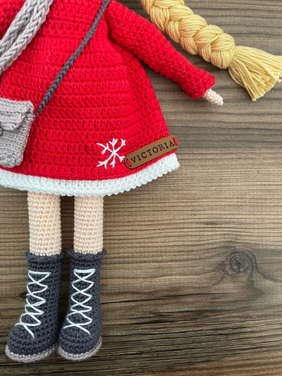 Handmade crocheted Red Snowflake Girl Doll featuring a red dress, snowflake detail, and a cute braided hairstyle. Customizable with a name on a leather label, made using amigurumi techniques. Perfect as a personalized gift or nursery decor.