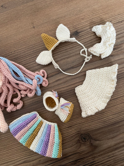 A handmade crocheted Unicorn Girl Doll with pastel rainbow dress, pink curly hair, and a golden horn. This amigurumi toy is customizable with a name on a leather label, perfect for nursery decor and personalized gifts.