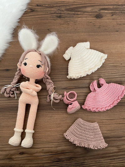 A handmade crocheted Rabbit Girl Doll with a pink dress, braided hair, and soft bunny ears. This amigurumi toy is customizable with a name on a leather label, making it a perfect choice for nursery decor and personalized gifts.