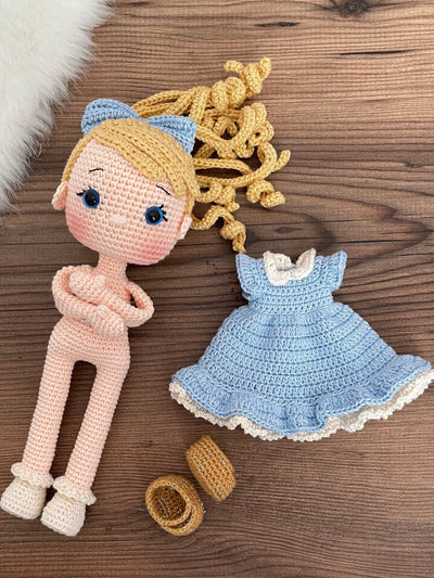 Handmade Blue Nina Doll with blonde hair, wearing a blue dress and a matching bow, made with 100% cotton yarn, customizable with a name on a leather label.