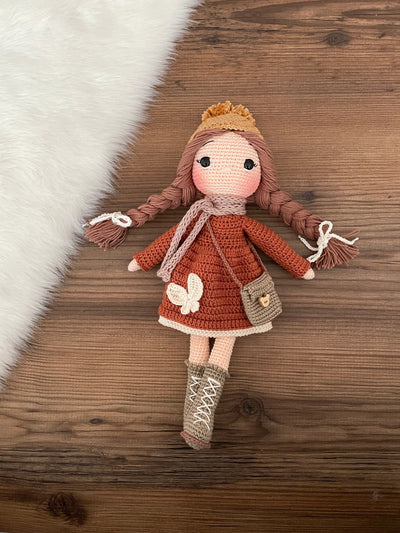 Handmade crochet winter girl doll in a brick-colored dress and hat, crafted with 100% cotton yarns. This amigurumi doll is customizable with a name on a leather label, making it a perfect, personalized gift for children and nursery decor.