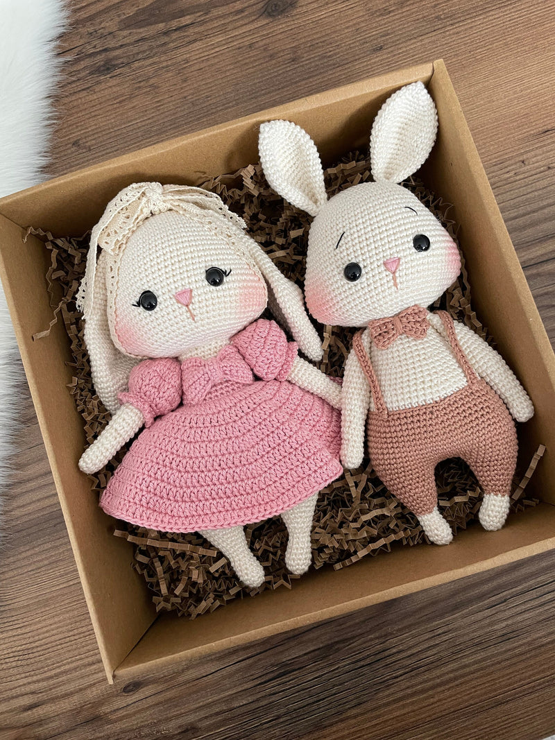 Handmade pink and brown bunny rabbit couple toy, lying inside a gift box, crocheted with amigurumi technique, personalized with names on leather labels, perfect for gifts and decor.