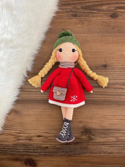 Handmade crocheted Red Snowflake Girl Doll featuring a red dress, snowflake detail, and a cute braided hairstyle. Customizable with a name on a leather label, made using amigurumi techniques. Perfect as a personalized gift or nursery decor.