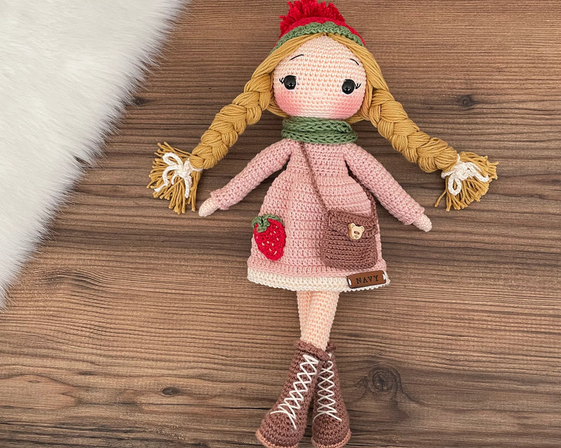 Handmade crocheted Strawberry Girl Doll featuring a pink dress, strawberry detail, and a cute braided hairstyle. Customizable with a name on a leather label, made using amigurumi techniques. Perfect as a personalized gift or nursery decor.