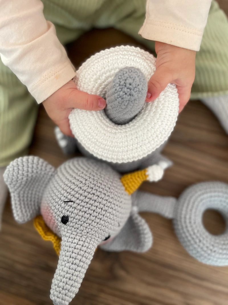 Handmade crocheted elephant educational toy with stackable rings, designed for Montessori learning. Features soft grey yarn, a yellow hat, and customizable name option.