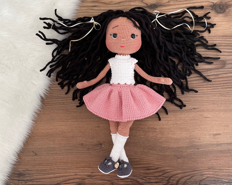 Handmade crocheted Pink Skirted Afro-American Doll with long brown hair, a cute skirt, customizable with a name on a leather label. Ideal for nursery decor and as a personalized gift.