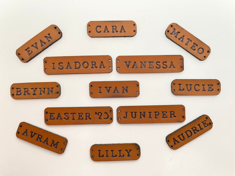 Custom leather name tags with various names displayed on a light background.