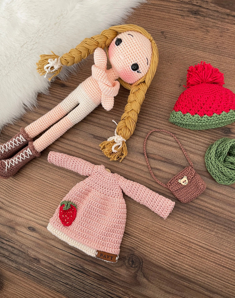 Handmade crocheted Strawberry Girl Doll featuring a pink dress, strawberry detail, and a cute braided hairstyle. Customizable with a name on a leather label, made using amigurumi techniques. Perfect as a personalized gift or nursery decor.