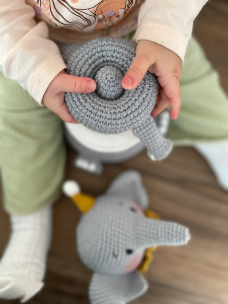 Handmade crocheted elephant educational toy with stackable rings, designed for Montessori learning. Features soft grey yarn, a yellow hat, and customizable name option.