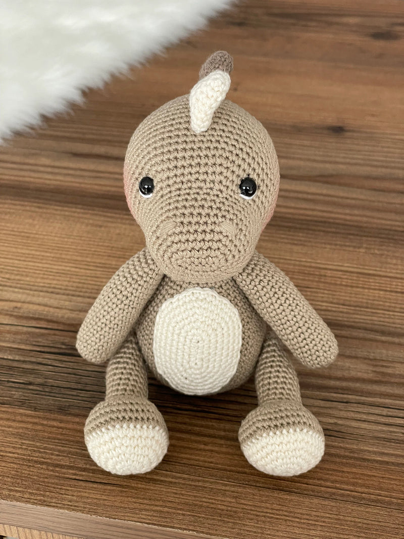 Handmade crochet dinosaur toy in shades of brown and beige, crafted with 100% cotton yarns. This amigurumi dinosaur is customizable with a name on a leather label, perfect for eco-friendly, personalized baby gifts and nursery decor.