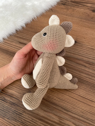 Handmade crochet dinosaur toy in shades of brown and beige, crafted with 100% cotton yarns. This amigurumi dinosaur is customizable with a name on a leather label, perfect for eco-friendly, personalized baby gifts and nursery decor.