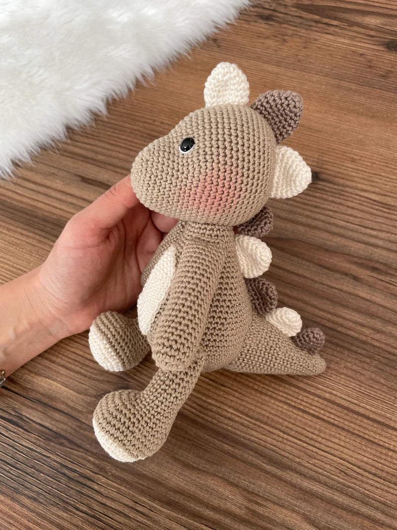 Handmade crochet dinosaur toy in shades of brown and beige, crafted with 100% cotton yarns. This amigurumi dinosaur is customizable with a name on a leather label, perfect for eco-friendly, personalized baby gifts and nursery decor.