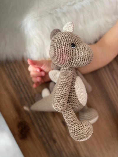 Handmade crochet dinosaur toy in shades of brown and beige, crafted with 100% cotton yarns. This amigurumi dinosaur is customizable with a name on a leather label, perfect for eco-friendly, personalized baby gifts and nursery decor.