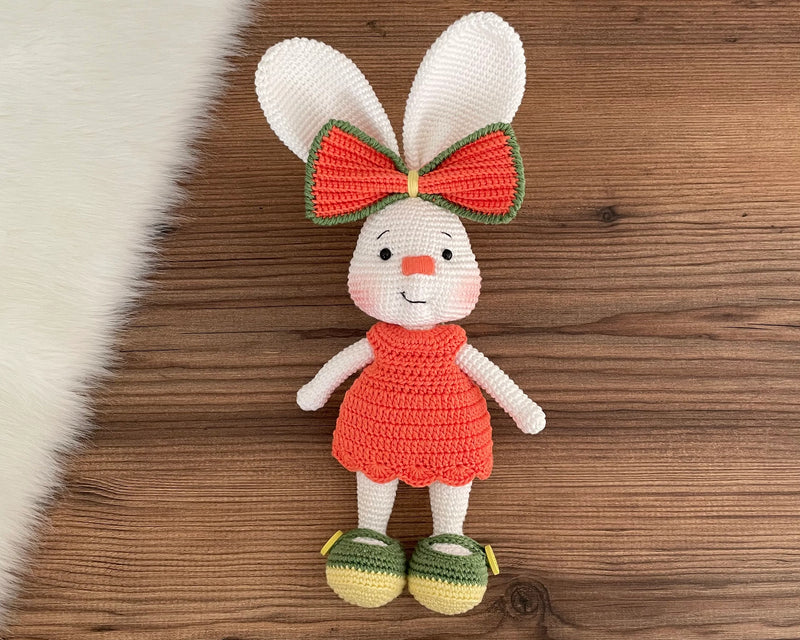 Handmade crocheted Orange Fancy Bunny Rabbit Toy in a bright orange dress with a large bow, customizable with a name on a leather label. Made using amigurumi techniques, this cute bunny is perfect for kids, nursery decor, or as a personalized gift.