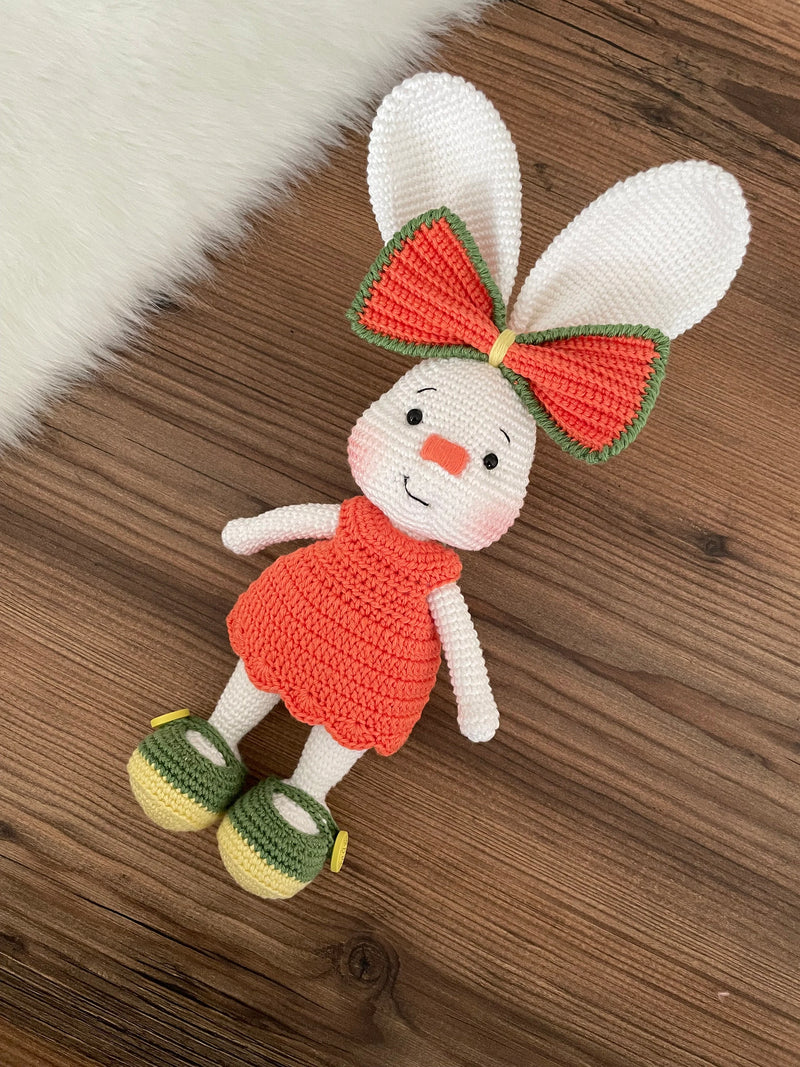 Handmade crocheted Orange Fancy Bunny Rabbit Toy in a bright orange dress with a large bow, customizable with a name on a leather label. Made using amigurumi techniques, this cute bunny is perfect for kids, nursery decor, or as a personalized gift.