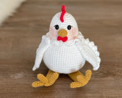 A handmade crocheted Chicken Toy with a cute and detailed design, featuring a red comb and yellow feet. This amigurumi toy is customizable with a name on a leather label, making it a perfect farm-themed nursery decor and personalized gift.