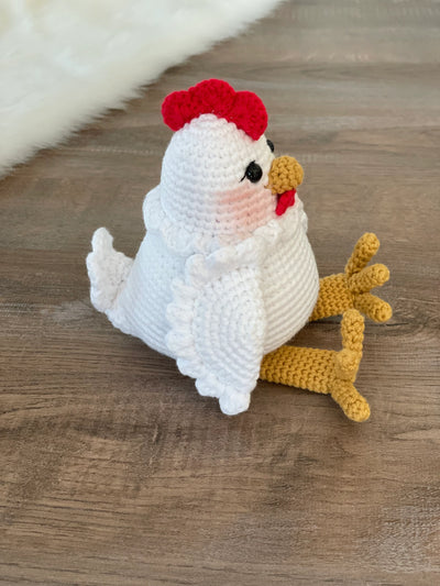 A handmade crocheted Chicken Toy with a cute and detailed design, featuring a red comb and yellow feet. This amigurumi toy is customizable with a name on a leather label, making it a perfect farm-themed nursery decor and personalized gift.