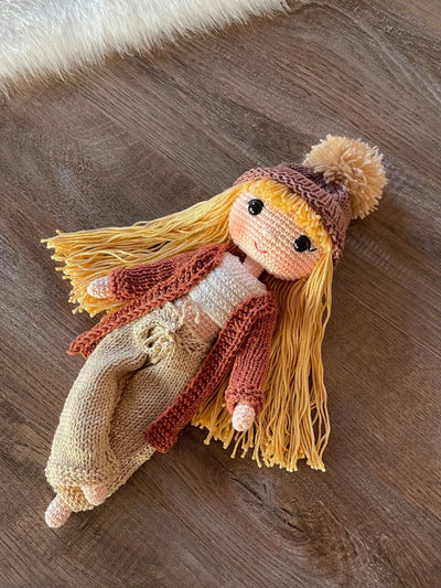 A handcrafted Brick Color Cardigan Cool Girl Doll with long brown hair, wearing a stylish brick color cardigan and beanie, crocheted using the amigurumi technique, and personalized with a custom name on a leather label.