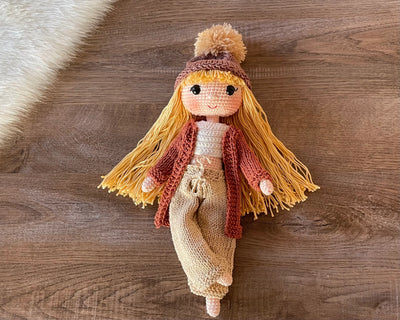 A handcrafted Brick Color Cardigan Cool Girl Doll with long brown hair, wearing a stylish brick color cardigan and beanie, crocheted using the amigurumi technique, and personalized with a custom name on a leather label.