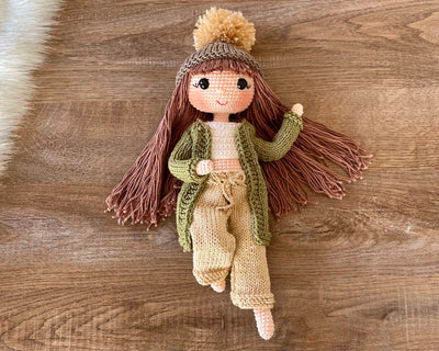 A handcrafted Green Cardigan Cool Girl Doll with long brown hair, wearing a stylish green cardigan and beanie, crocheted using the amigurumi technique, and personalized with a custom name on a leather label.