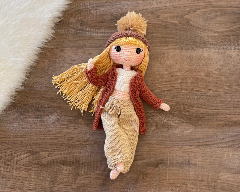 A handcrafted Brick Color Cardigan Cool Girl Doll with long brown hair, wearing a stylish brick color cardigan and beanie, crocheted using the amigurumi technique, and personalized with a custom name on a leather label.