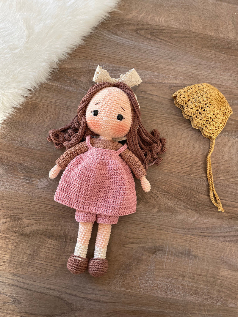 Handmade village girl doll crocheted using the amigurumi technique. Dressed in a rustic pink outfit with a bonnet, this personalized doll features a custom name on a leather label. Perfect for collectors and kids.