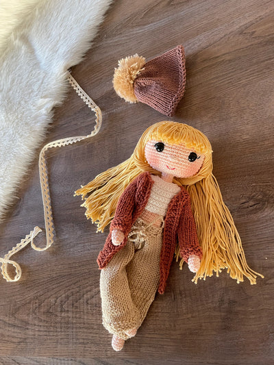 A handcrafted Brick Color Cardigan Cool Girl Doll with long brown hair, wearing a stylish brick color cardigan and beanie, crocheted using the amigurumi technique, and personalized with a custom name on a leather label.