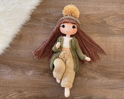 A handcrafted Green Cardigan Cool Girl Doll with long brown hair, wearing a stylish green cardigan and beanie, crocheted using the amigurumi technique, and personalized with a custom name on a leather label.