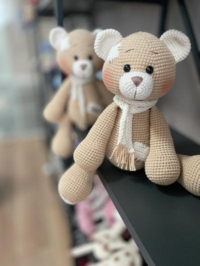 A handmade beige teddy bear toy crafted with the amigurumi technique, featuring a soft texture, a personalized leather name patch, and a cute, cuddly design.