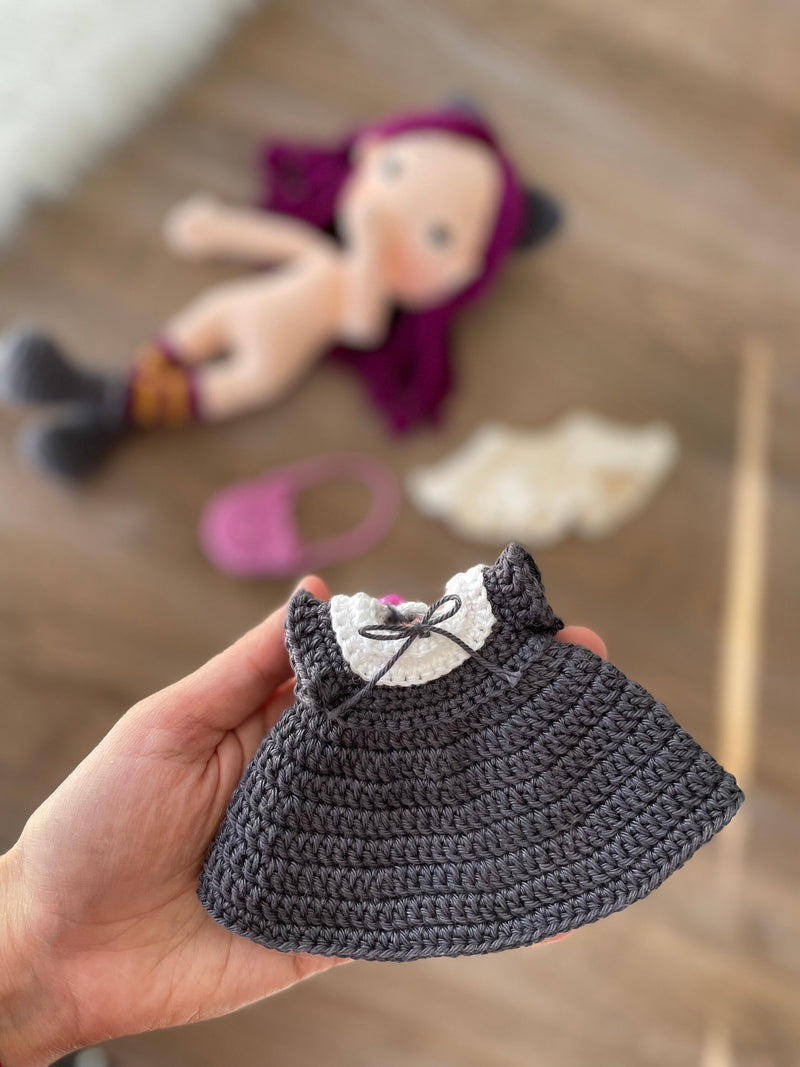 A handcrafted Cat Girl Doll with rich purple hair, wearing a dark dress with cat ears and holding a pink cat-shaped purse. The doll is crocheted using the amigurumi technique and personalized with a custom name on a leather label.