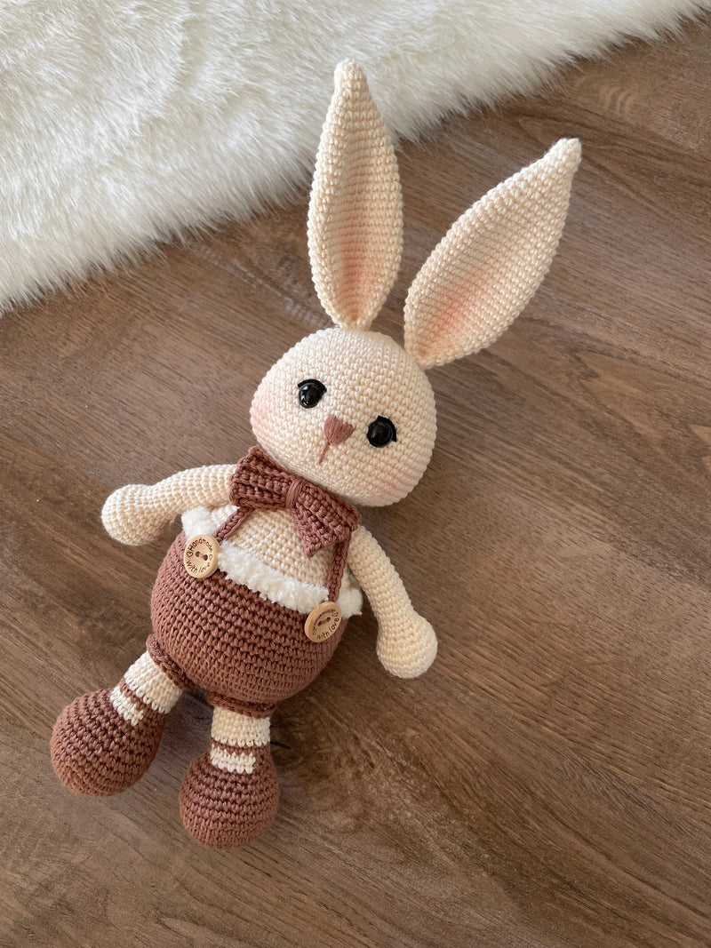 A handmade crocheted Chubby Boy Bunny Rabbit Toy wearing a bow tie and overalls, made with love and care. This amigurumi toy is customizable with a name on a leather label, perfect for nursery decor and personalized baby gifts.