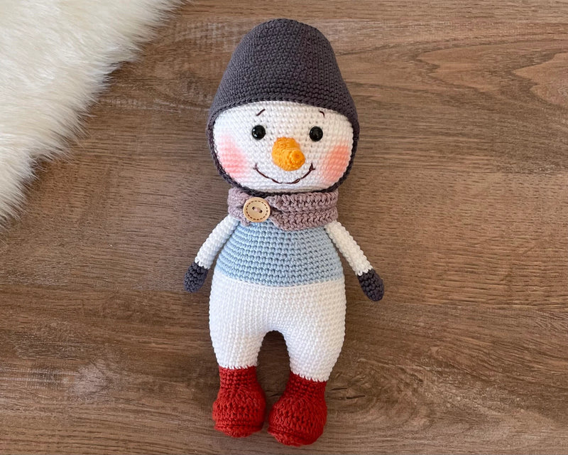 Handmade crocheted snowman toy with red boots, customizable with a name on a leather label, made using amigurumi techniques, perfect as a holiday gift or decor.