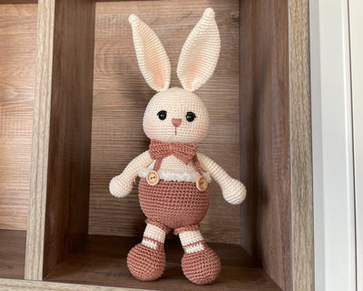 A handmade crocheted Chubby Boy Bunny Rabbit Toy wearing a bow tie and overalls, made with love and care. This amigurumi toy is customizable with a name on a leather label, perfect for nursery decor and personalized baby gifts.