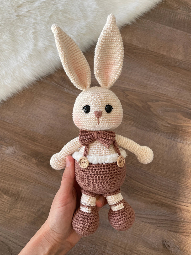 A handmade crocheted Chubby Boy Bunny Rabbit Toy wearing a bow tie and overalls, made with love and care. This amigurumi toy is customizable with a name on a leather label, perfect for nursery decor and personalized baby gifts.