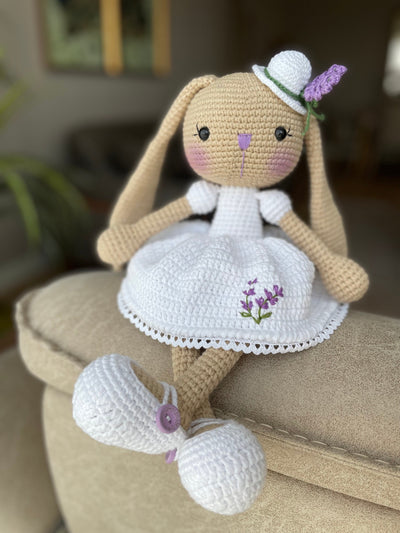 Handmade crocheted Lavender Flower Dressed Bunny Rabbit Toy, complete with a matching hat. This customizable toy includes a name on a leather label and is made using amigurumi techniques. Perfect for nurseries or as a personalized gift.